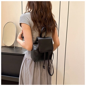 Detailed view of a minimalist black mini backpack with flap closure and adjustable straps