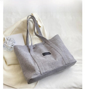 Detail of grey canvas tote bag featuring a black fashion label on a textured fabric