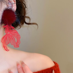 Macro shot of red pompom and hollow metal carp earring on a female model