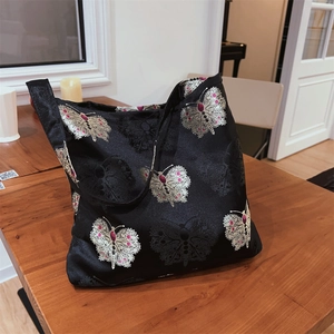 Detail view of exquisite silver butterfly embroidery on a black satin jacquard tote bag