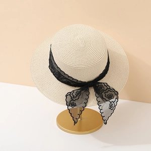 Elegant beige straw boater hat with black floral lace bow on a golden display stand