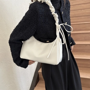 Minimalist ivory shoulder bag with pleated strap and decorative bow detail shown on model