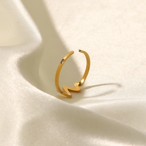 Macro view of gold-plated zigzag heartbeat ring on white silk fabric background