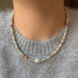 Detail of beaded necklace with freshwater pearl and thin gold chain on a sweater
