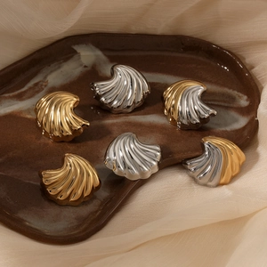 Golden and silver stainless steel shell earrings on beige tulle in a ceramic tray