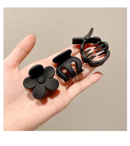 Detailed view of three matte black hair claws including flower and geometric shapes