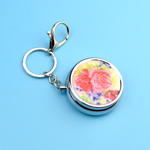 Portable round metal keychain pill box with floral peony pattern on blue background