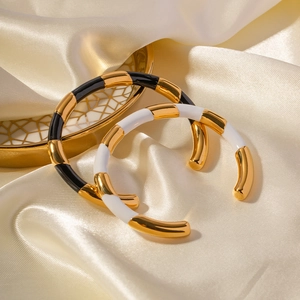 Detail of open titanium steel bangles in black and white enamel on a gold silk fabric