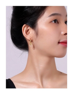 Detailed close-up of a gold heart drop earring with sparkling zircon stones on a model