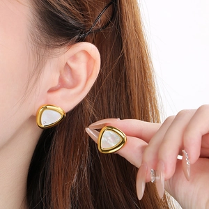 Triangle shell stud earrings in gold stainless steel worn by a model in close-up