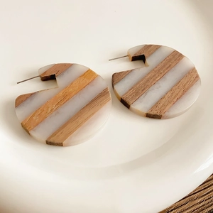 Detailed close-up of C-shaped wood and resin earrings with striped texture on white plate