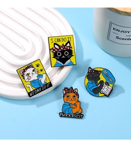 Set of four cartoon cat enamel pins with motivational quotes on a blue surface
