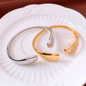 Minimalist 18K gold and silver plated open bangles with teardrop ends on a plate