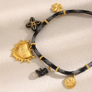 Détail du bracelet en corde tressée avec cœur doré 18K, trèfle et breloques noires