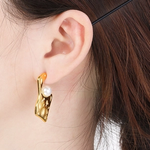 Detail of gold hammered earrings featuring a white pearl on an elegant female model