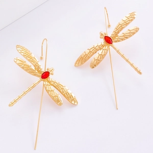 Détail de boucles d'oreilles libellule dorées avec gemmes rouges et ailes texturées