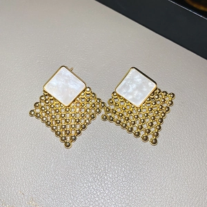 Detail of woven geometric stud earrings in vintage gold with white pearl inlay