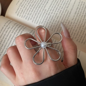 Detailansicht eines silbernen Blumenrings mit Perle auf ästhetischem Buchhintergrund