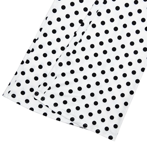 Gros plan du bas d'un pantalon évasé blanc à pois noirs en tissu lisse et doux