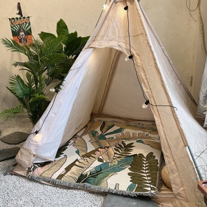 Detail of bohemian indoor teepee tent featuring tropical leaf mat and warm string lights