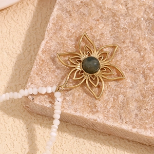 Detail of 18K gold petal pendant with dark green stone on white beaded necklace