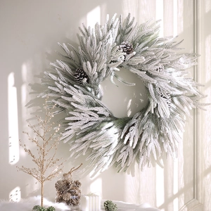 Christmas wreath with flocked pine needles and pine cones on a wall with window shadows