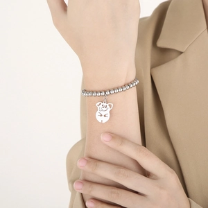 Close-up of a silver beaded pig charm bracelet worn on a wrist with a beige blazer