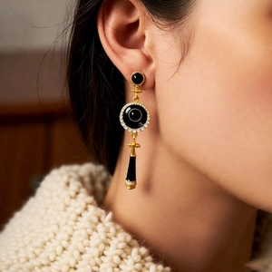 Close-up of vintage gold drop earrings with black enamel and sparkling zircons on a model