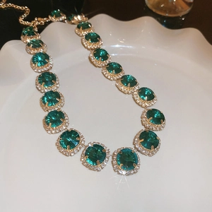 Detail of gold necklace featuring oval green gemstone and crystal rhinestones