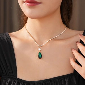 Close-up of model wearing gold necklace with green teardrop zircon and clear stone pendant