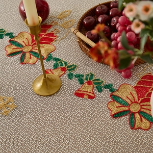 Close-up of beige Christmas tablecloth with embroidered golden bells and red bows