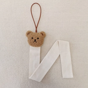 Detail of cute brown plush bear charm on white woven strap for hair accessory storage