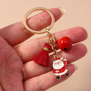 Hand holding Christmas keychain with gold ring, red tassel, bell and Santa Claus pendant