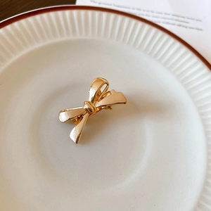 Detailed close-up of a glossy gold metal bow hair clip on a white ceramic tray
