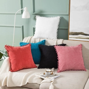 Close-up of colorful velvet pillow covers with pom-pom tassels on a cozy beige sofa