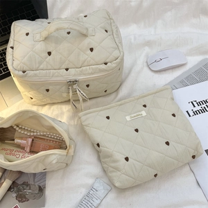 Detail of cream quilted makeup bag featuring heart embroidery and portable handle design