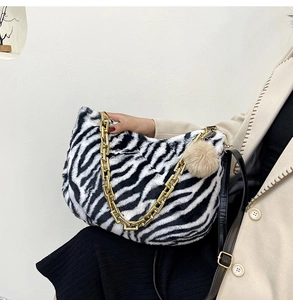 Detail of zebra pattern plush tote bag with gold chain strap and beige pompom charm