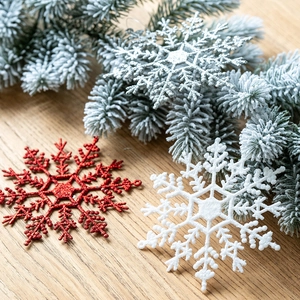 Fiocchi di neve natalizi scintillanti in rosso, bianco e argento su rami di pino