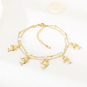 Close-up of a double-layered gold dolphin anklet with white pearls on a beach background