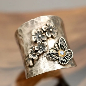 Vintage silver wide ring featuring embossed flowers and a blue gem butterfly on wood