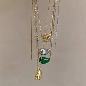 Detailed view of teardrop pendants in gold, silver, and green stone on delicate chains