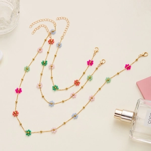 Detailed macro shot of gold beaded necklaces with colorful floral charms on beige fabric