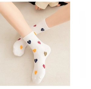 Close-up of white calf socks with colorful heart patterns worn on feet by model