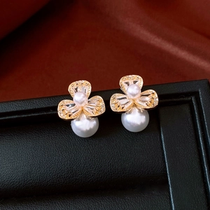Detail of floral gold earrings featuring baguette zircons and white dangling pearls