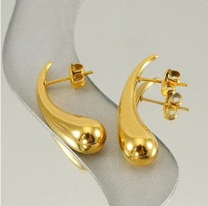 Macro shot of gold teardrop earrings with mirror polish on a reflective surface