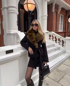 Detail of elegant black wool coat featuring a plush brown faux fur collar and waist belt