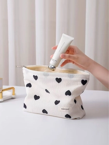 Portable white fabric cosmetic bag with black heart patterns and branded woven label
