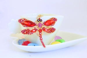 Detailed view of red crystal dragonfly charm on a white cup with golden accents