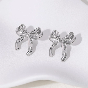 Close-up of minimalist silver bow stud earrings on a clean white aesthetic surface