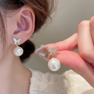 Close-up of gold butterfly stud earrings with sparkling crystals and drop pearls